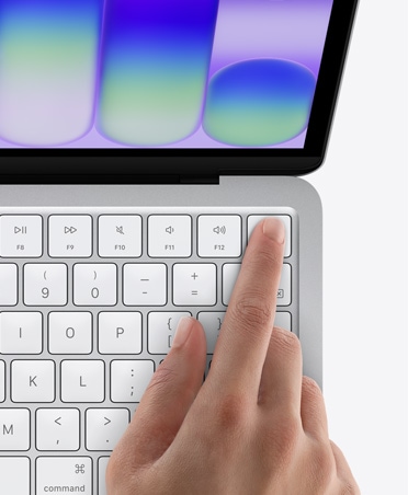 MacBook Neo, цвят сребърно, пръст на човек върху сензора Touch ID в горния десен ъгъл на клавиатурата
