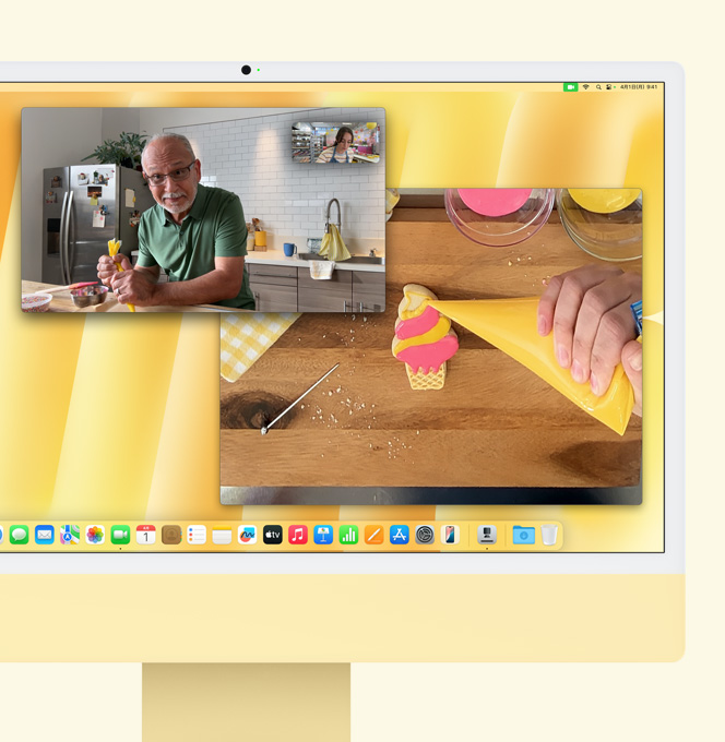 イエローのiMac。デスクビューのデモ。菓子を作っている人がもう一人の人とビデオ通話をしている。1つの画面には菓子を作っている男性の顔が、もう1つの画面にはクッキーをアイシングしている手が表示されている