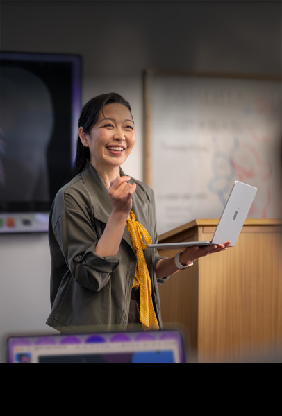 講堂でシルバーのMacBookを手に持ち、学生にプレゼンテーションしている大学教師。パフォーマンスの高さと長いバッテリー駆動時間を示している