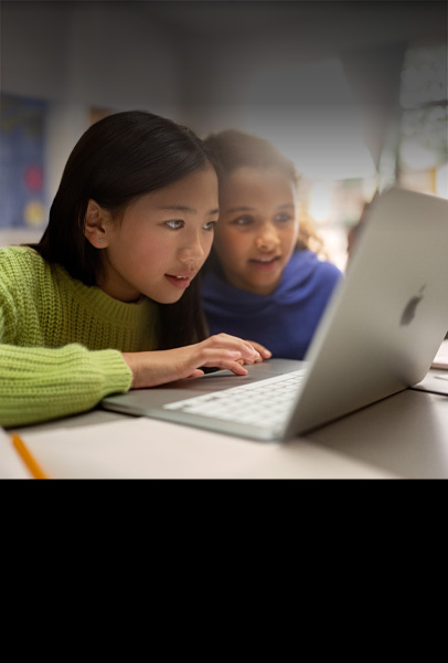 教室で席につき、MacBookを熱心に見ながら共同作業する2人の子ども