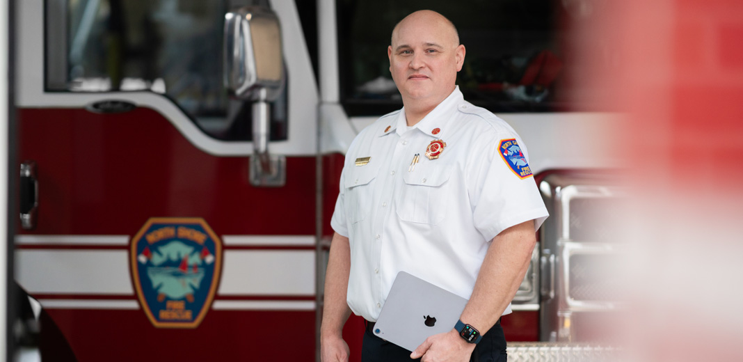 Chefe dos bombeiros em frente a um caminhão, segurando um iPad e usando um Apple Watch