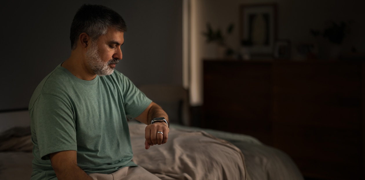 Ein Mann, der im Bett sitzt und auf seine Apple Watch schaut.