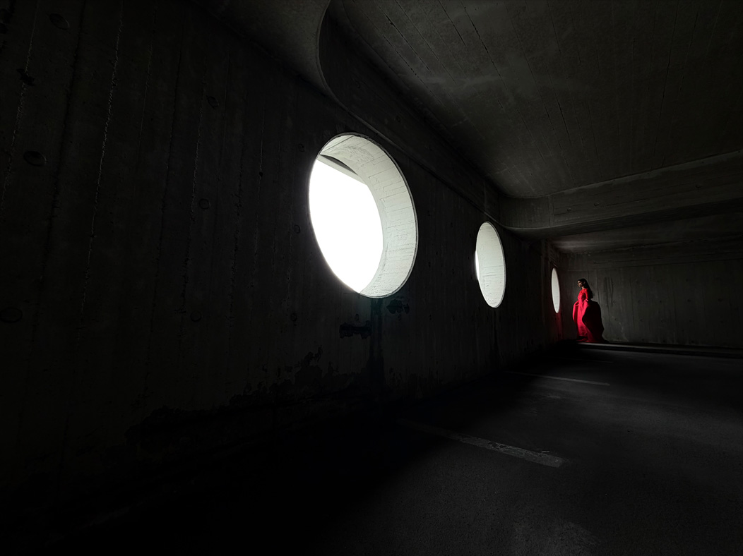 Une femme vêtue d’une longue robe rouge se fait photographier dans une pièce vide. L’app Appareil photo change de distance focale pour illustrer les capacités du système caméra pro, mettant en valeur: 13 mm