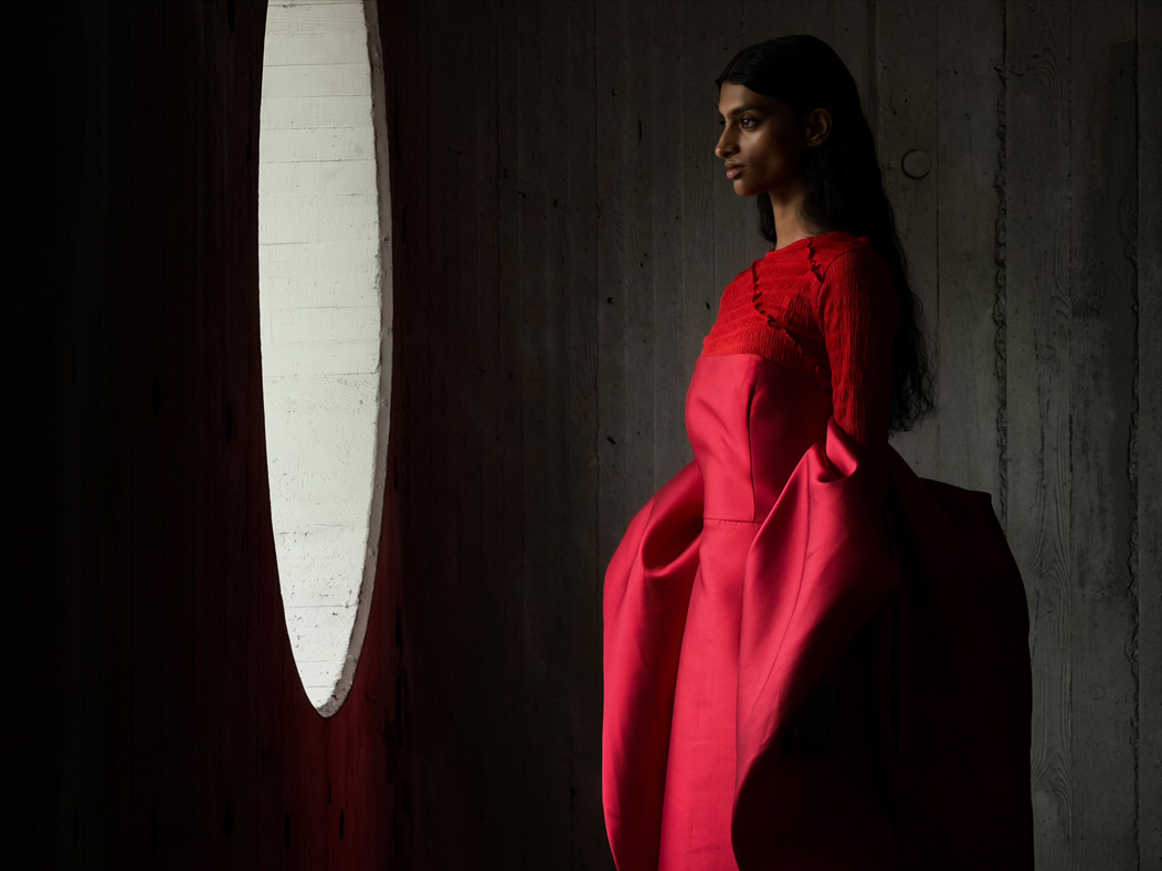 Une femme vêtue d’une longue robe rouge se fait photographier dans une pièce vide. L’app Appareil photo change de distance focale pour illustrer les capacités du système caméra pro, mettant en valeur: 200 mm