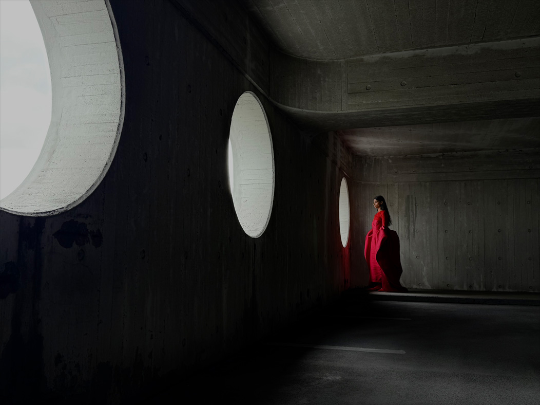 Une femme vêtue d’une longue robe rouge se fait photographier dans une pièce vide. L’app Appareil photo change de distance focale pour illustrer les capacités du système caméra pro, mettant en valeur: 35 mm