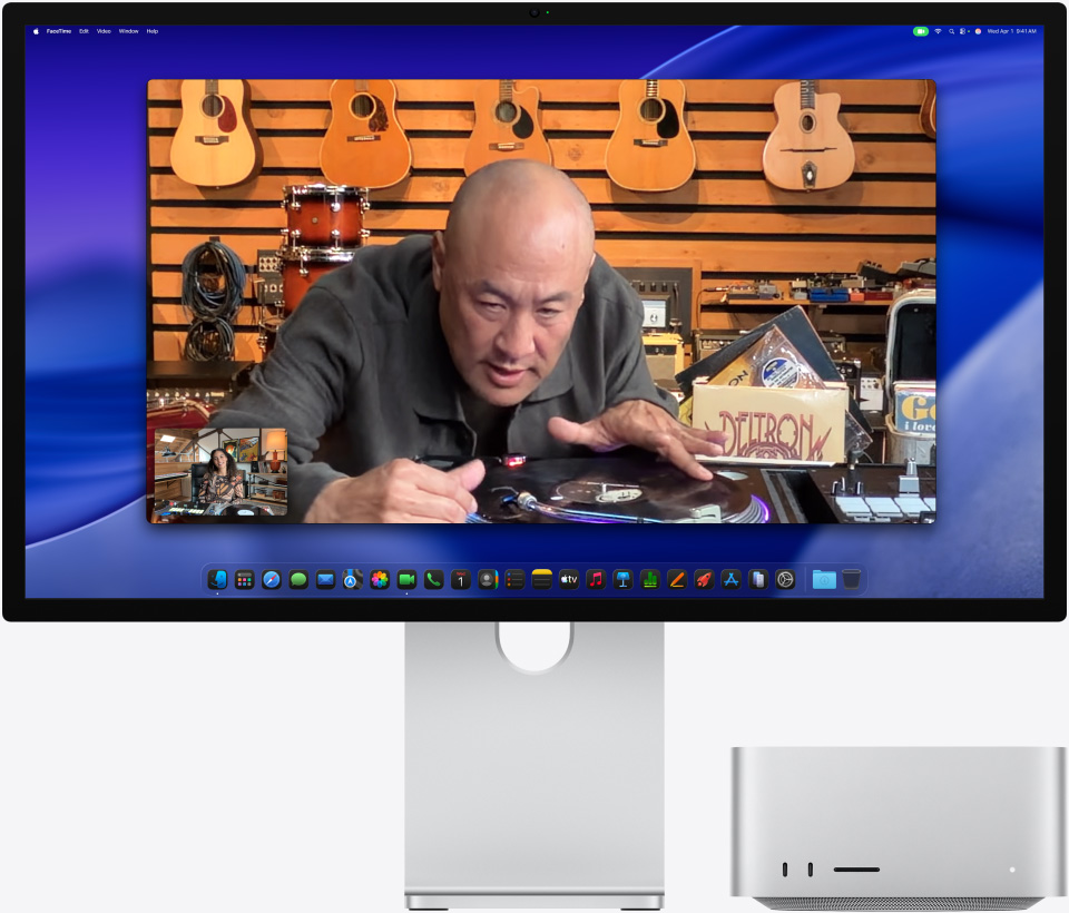 Una persona en una tienda de música mira de cerca un tocadiscos durante una videollamada en un monitor Studio Display XDR con un Mac Studio debajo